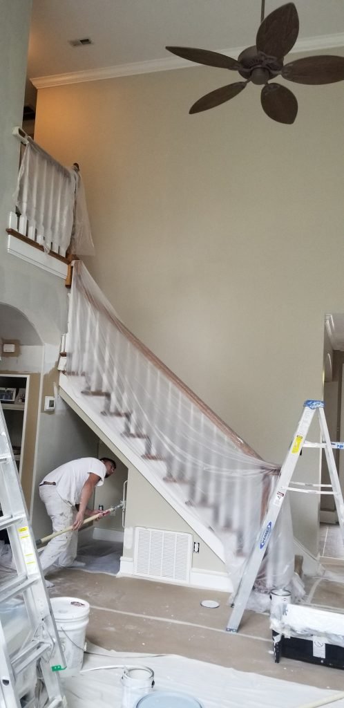 Professional painter working on a high-ceiling staircase area with precise wall painting by Dubon Painting and More Inc.