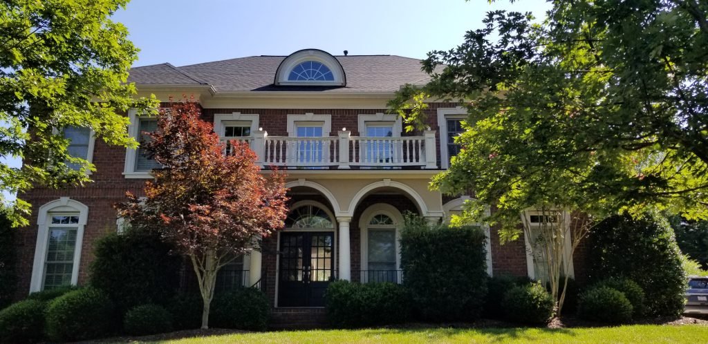 Beautifully painted exterior of a two-story house by a painting company in Charlotte, NC, surrounded by lush greenery.