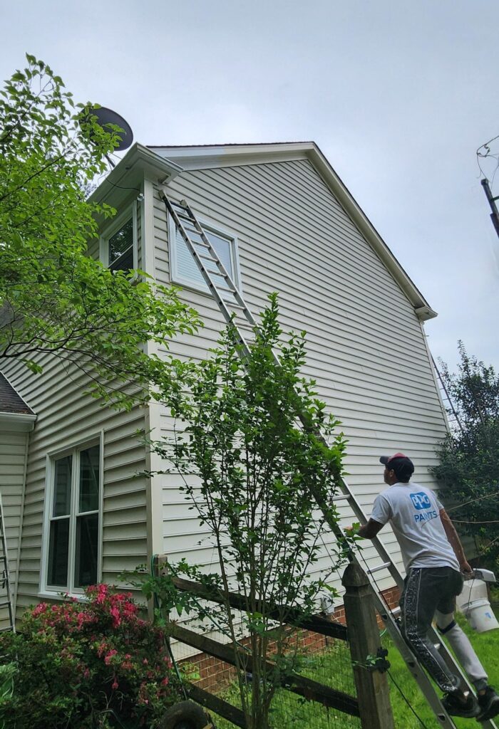 House exterior being painted by house painters in Charlotte, NC, showcasing a worker on a ladder ensuring precision.