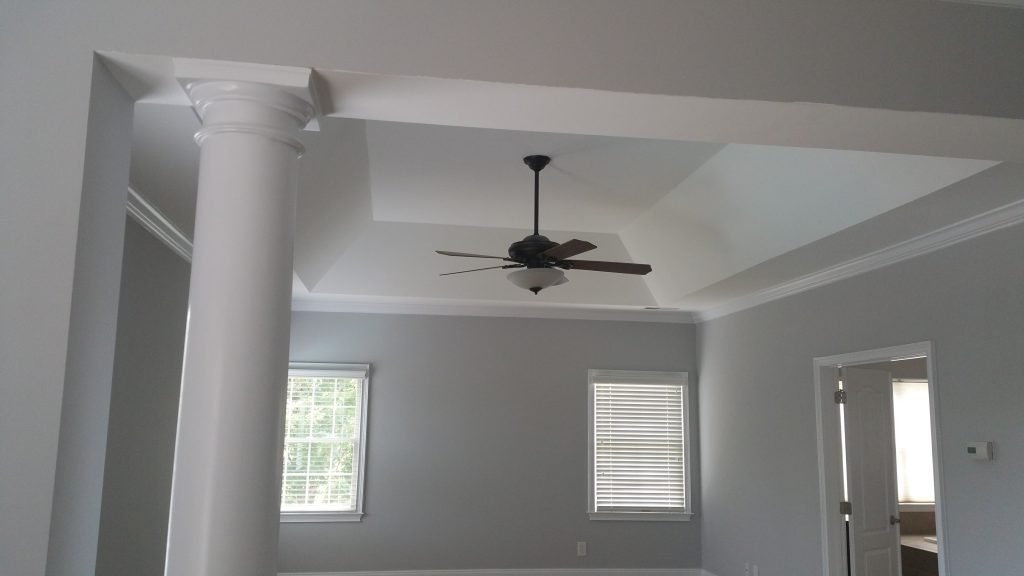 Bright room with light gray walls, a ceiling fan, and decorative pillars, featuring recent drywall repair in Charlotte, NC.