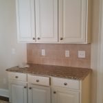 White kitchen cabinets with a beige backsplash, showcasing expert cabinet painting in Charlotte, NC.