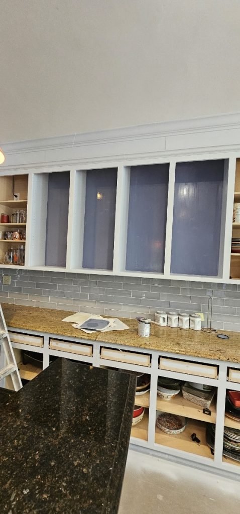 Kitchen cabinets in the process of being painted, with open shelving and a backsplash, highlighting cabinet painting in Charlotte, NC.