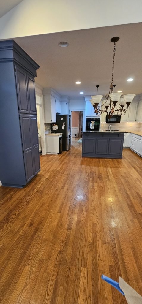 Spacious kitchen with hardwood floors, a dark blue island, and painted cabinetry, highlighting cabinet painting in Charlotte, NC.