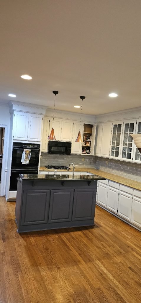 Modern kitchen with a dark island and white cabinets, showcasing expert cabinet painting in Charlotte, NC.